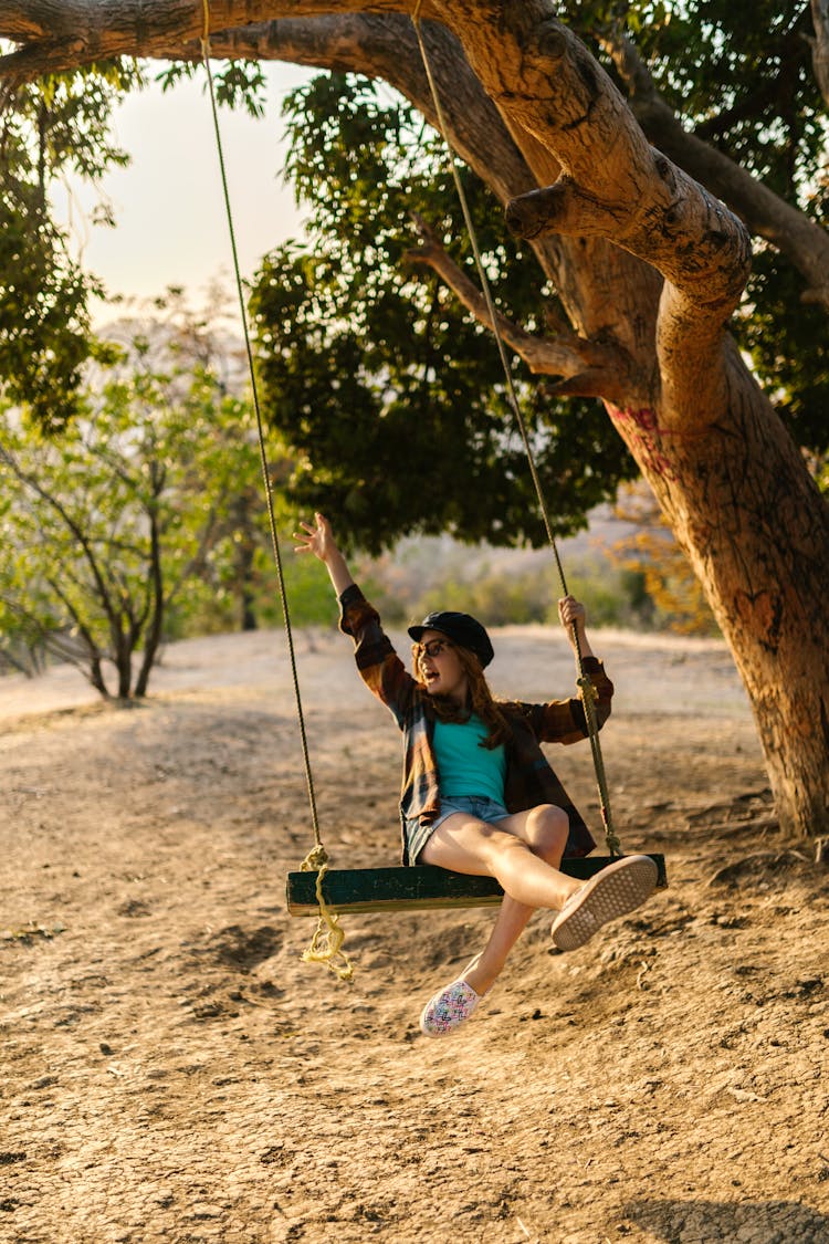 A Girl Riding A Swing Under A Tree