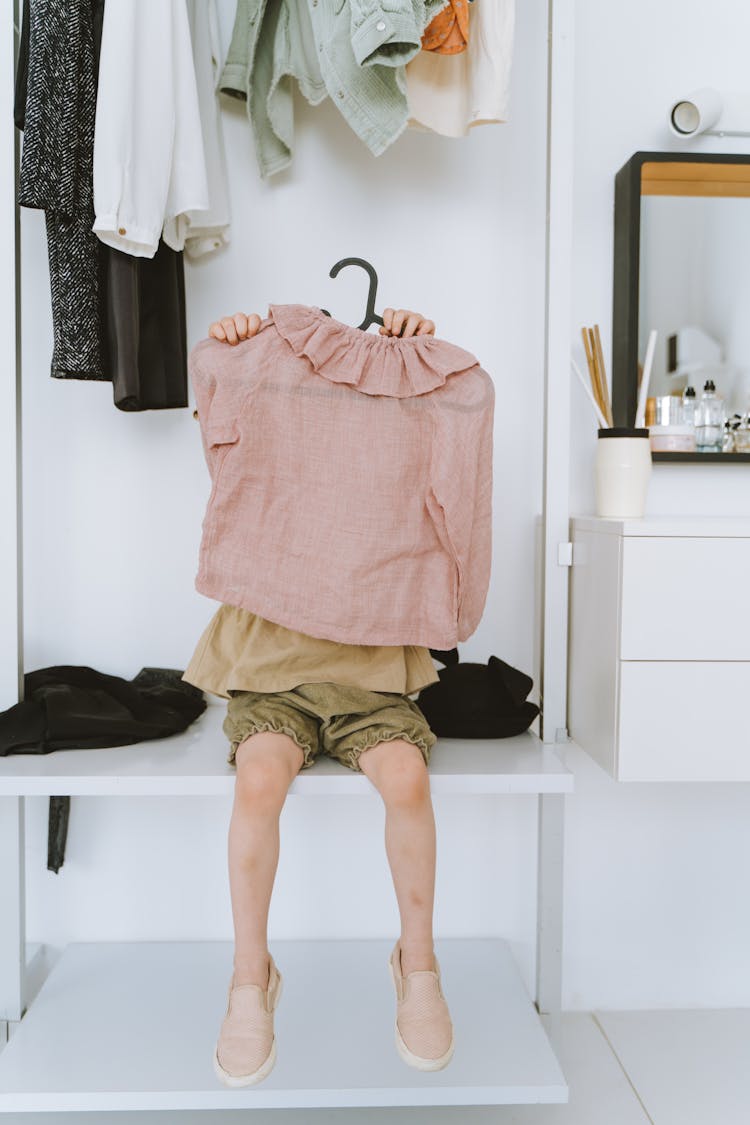 A Kid Sitting On A Cabinet While Holding A Pink Blouse