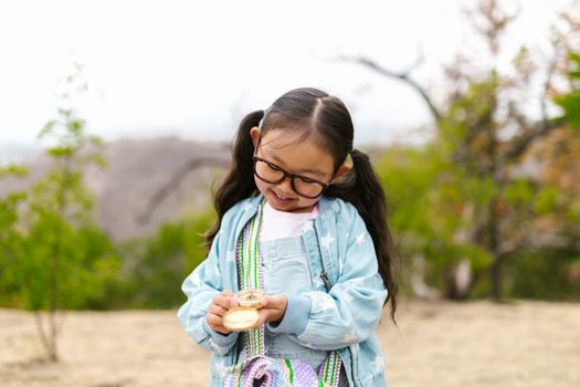 Charming young girl with glasses holding a compass outdoors, smiling.
