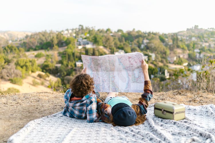 Couple Lying On Picnic Blanket While Looking At A Map