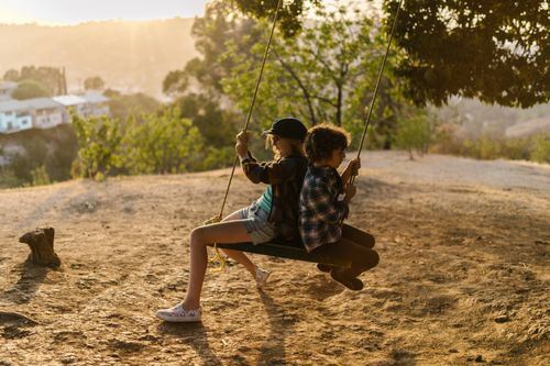 Free Two kids joyfully swinging together in a sunny park setting. Stock Photo