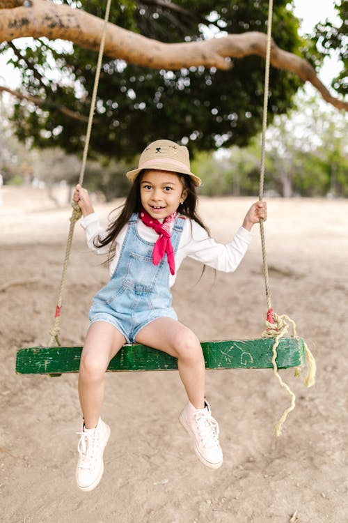 Girl in White Shirt and Denim Jumper Sitting on a Swing