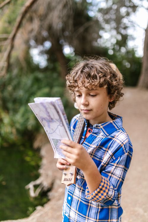 Free Curly-haired boy joyfully studies a map on a nature trail, embracing adventure. Stock Photo