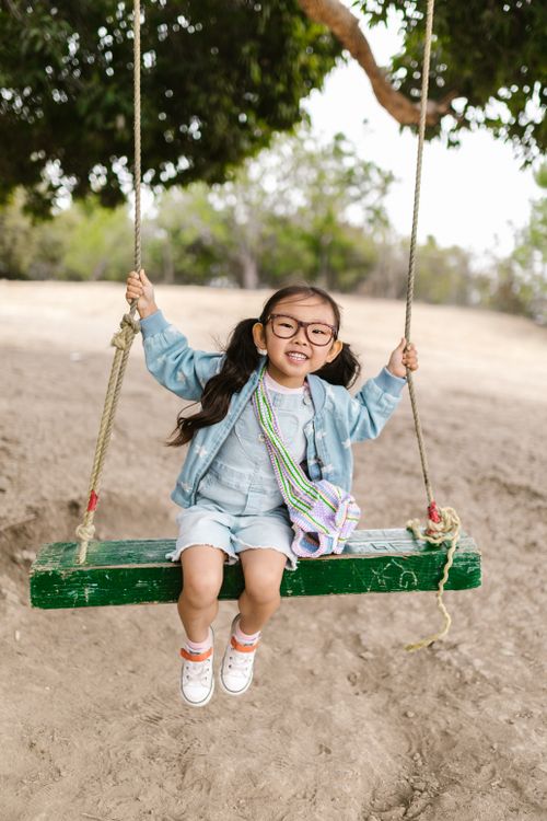 Free A happy young girl enjoying a swing outdoors in a sunny park setting. Stock Photo