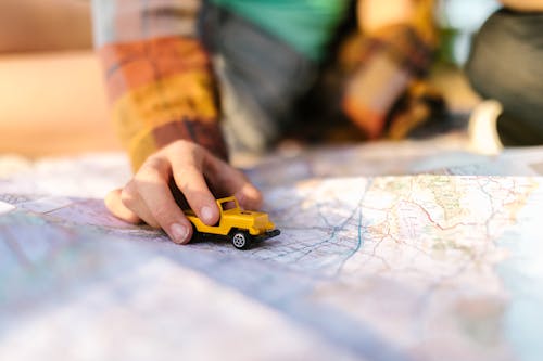Person Holding Yellow and Black Plastic Toy Car on a Map