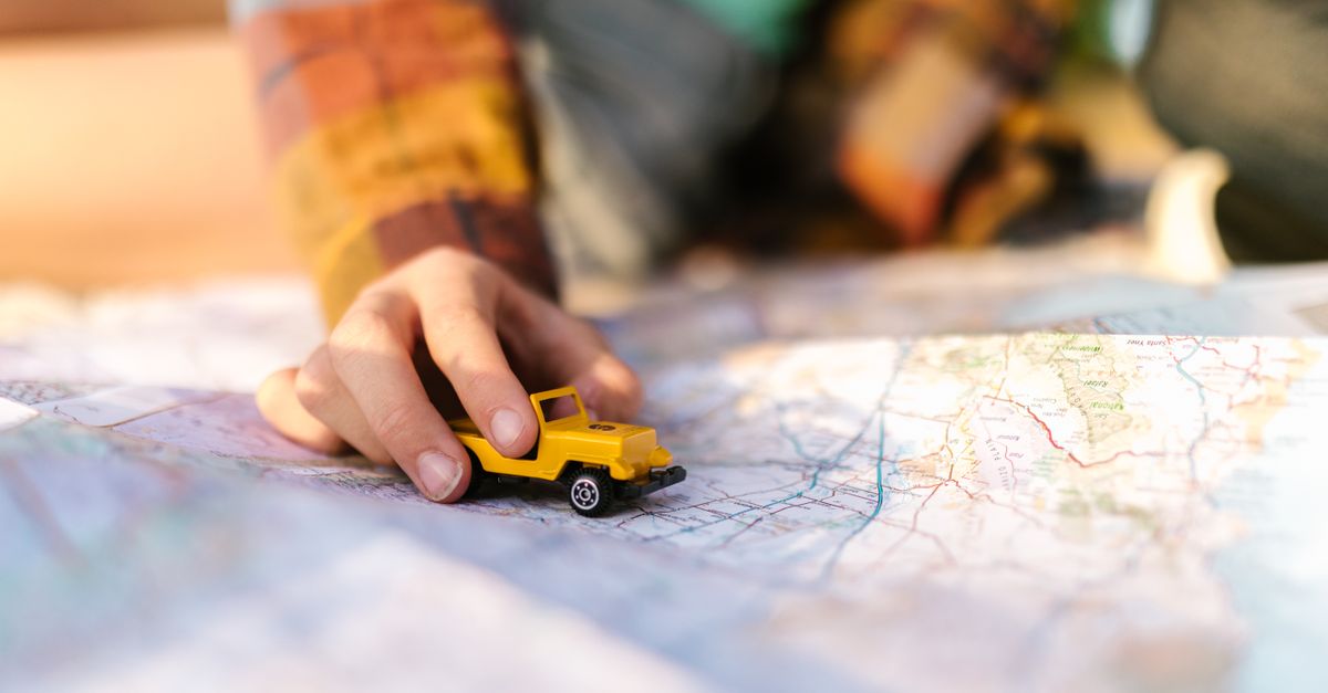 Close-up of a hand with a yellow toy car on a map, symbolizing travel planning.