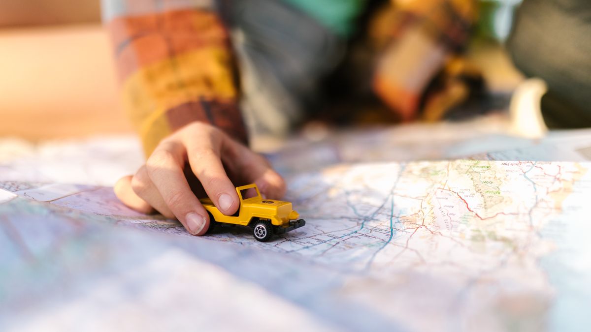 Close-up of a hand with a yellow toy car on a map, symbolizing travel planning.