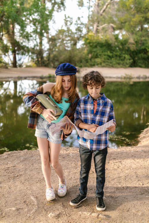 Free Two children by a lake, exploring with a map and binoculars. Outdoor adventure. Stock Photo