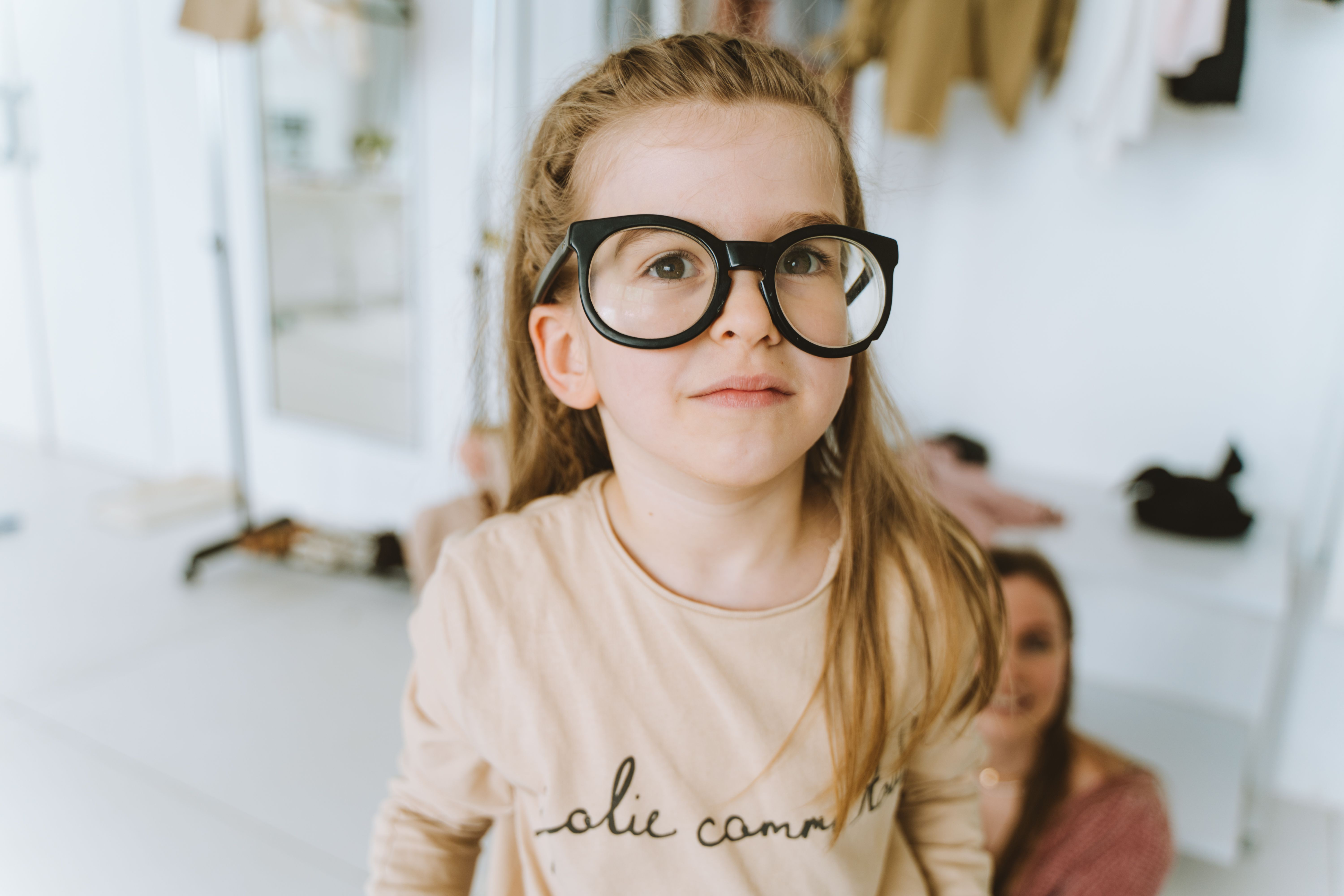 Adorable young girl with oversized glasses smiling indoors, showcasing fashion and fun.