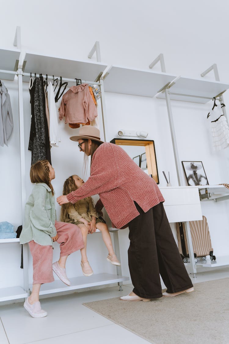 A Woman In Red Sweater Standing Beside Girls Sitting On Closet Shelf