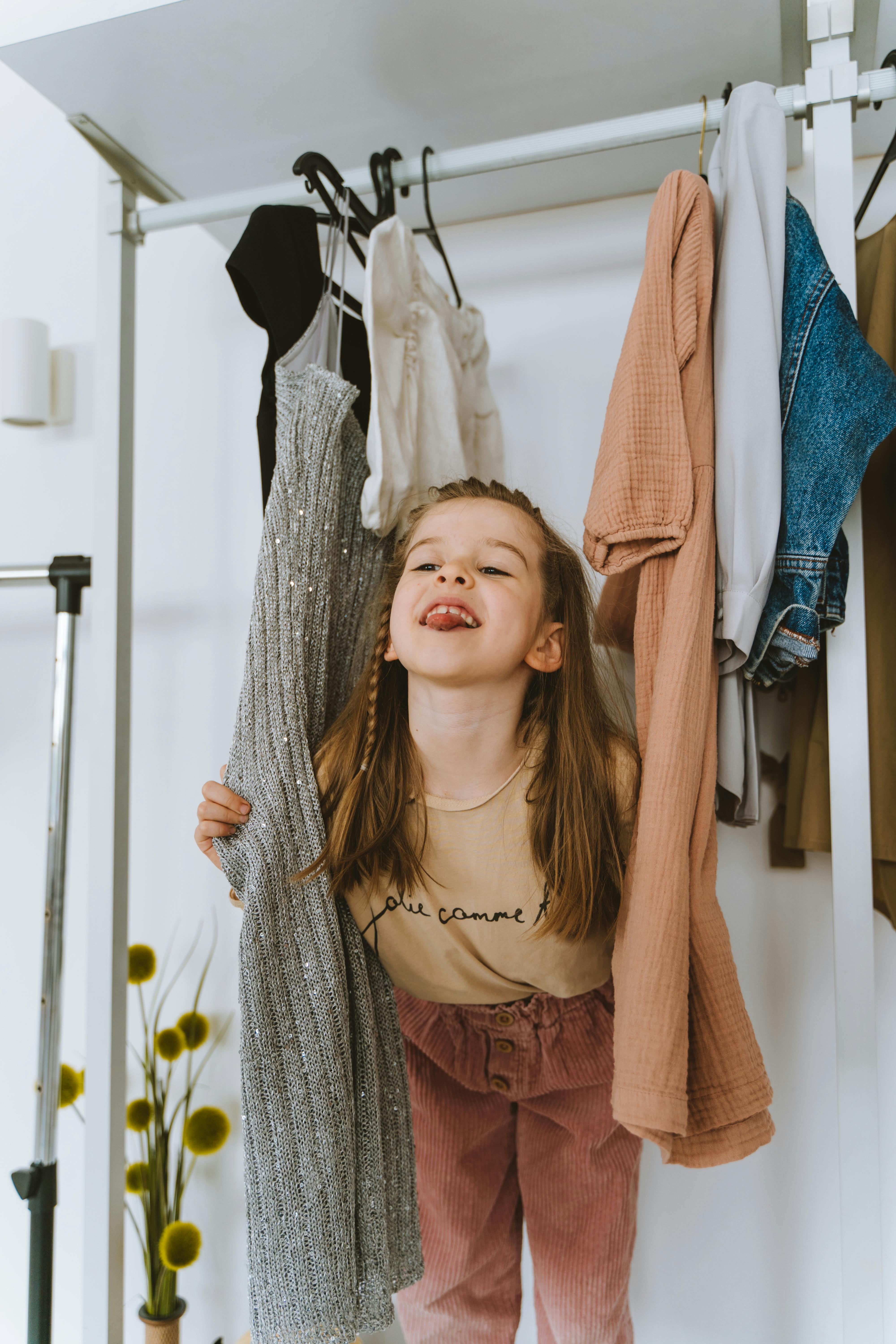 Adorable child playing amidst hanging clothes in closet.