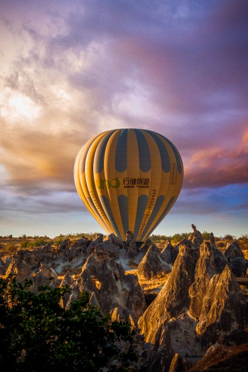 Free Amazing view of yellow hot air balloon located in rocky valley under cloudy colourful purple sky in Cappadocia Stock Photo
