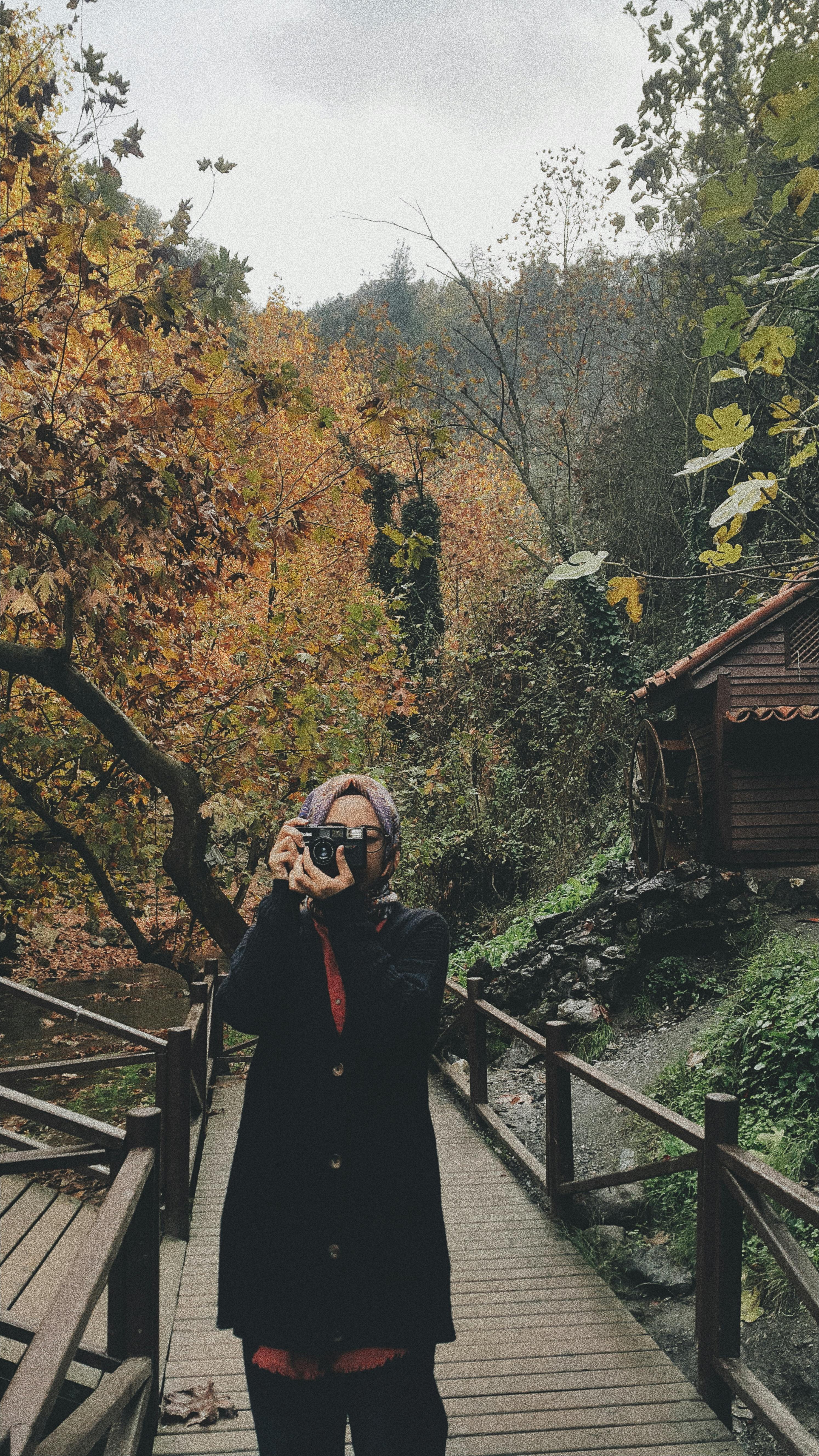A woman enjoys her photography hobby on a scenic autumn path, capturing the natural beauty with her camera.
