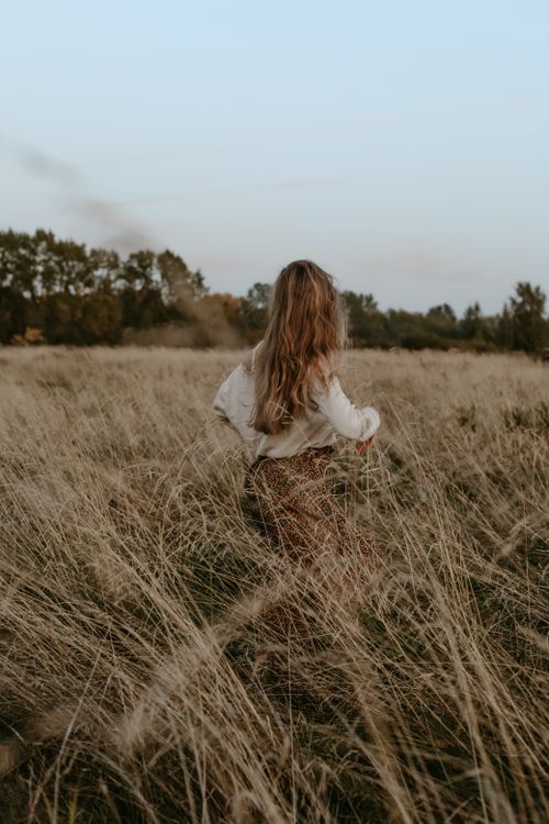 Free A woman with long hair walks through a grassy field at sunset, evoking freedom and tranquility. Stock Photo