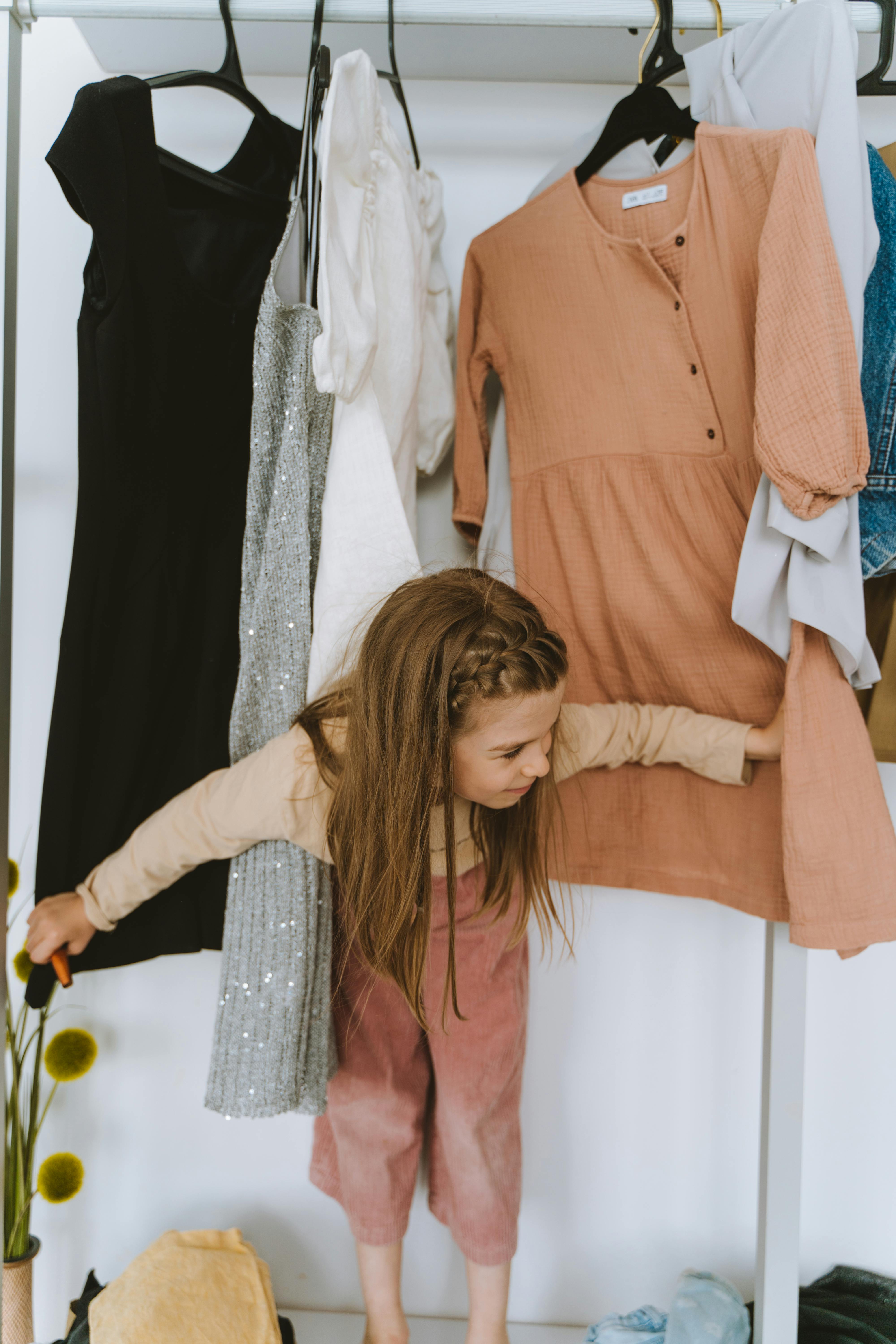 A young girl curiously explores a vibrant collection of dresses in a stylish indoor wardrobe.