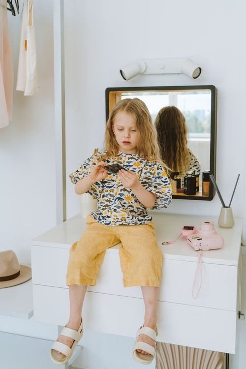 Free Young girl with blonde hair sitting on a dresser playing thoughtfully indoors. Stock Photo