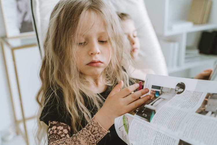 A Young Girl In Black Shirt Holding A Magazine