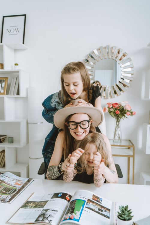 Free Happy family scene with mother and daughters enjoying books and laughter in a cozy room. Stock Photo