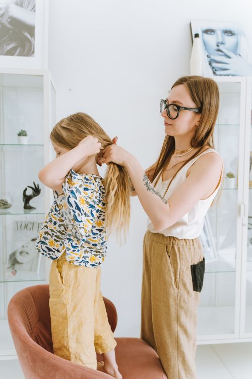 Free A mother braids her daughter's hair in a modern room with magazine decor. Indoors, warm atmosphere. Stock Photo