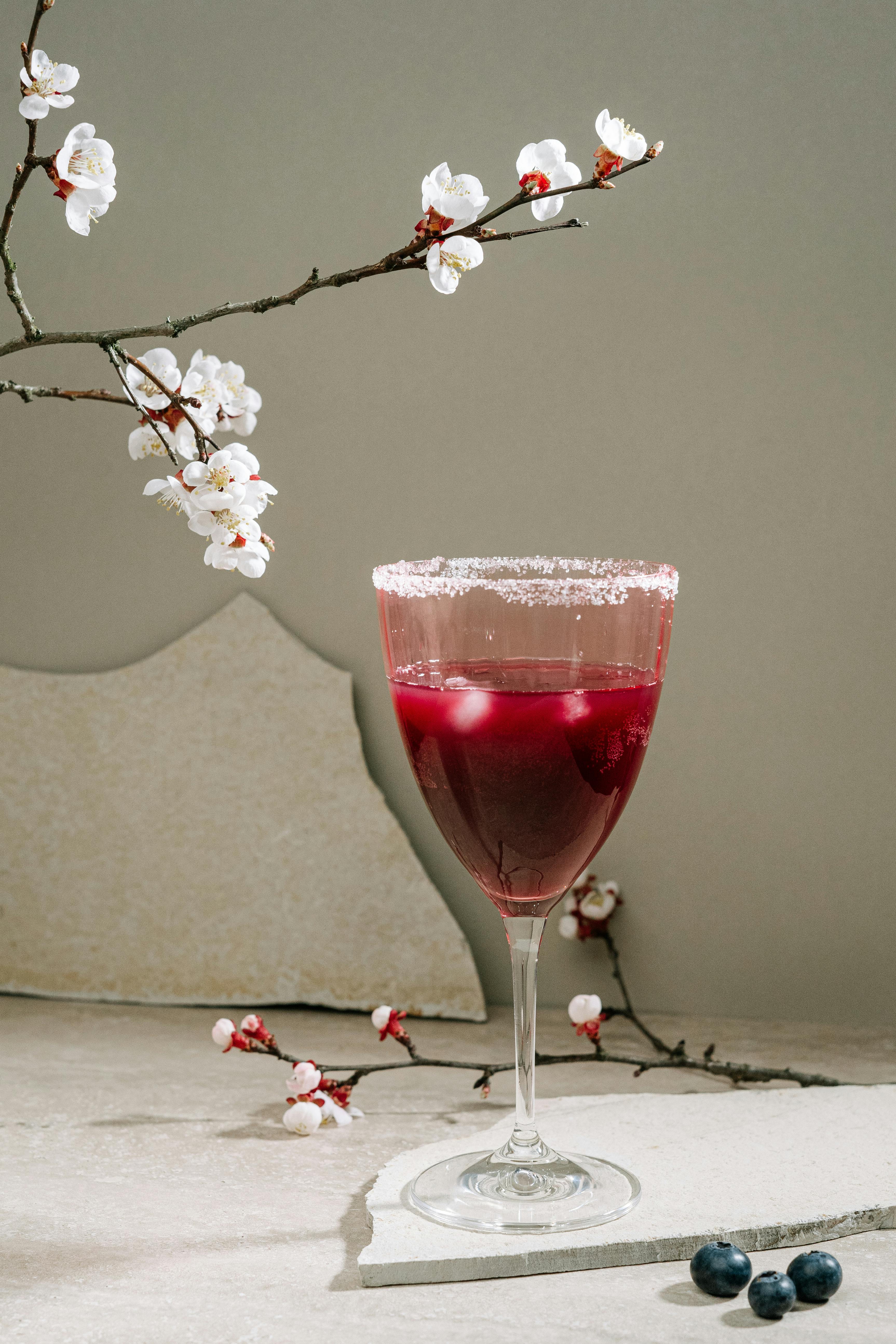 glass with an alcoholic drink with a cherry blossom branch next to it