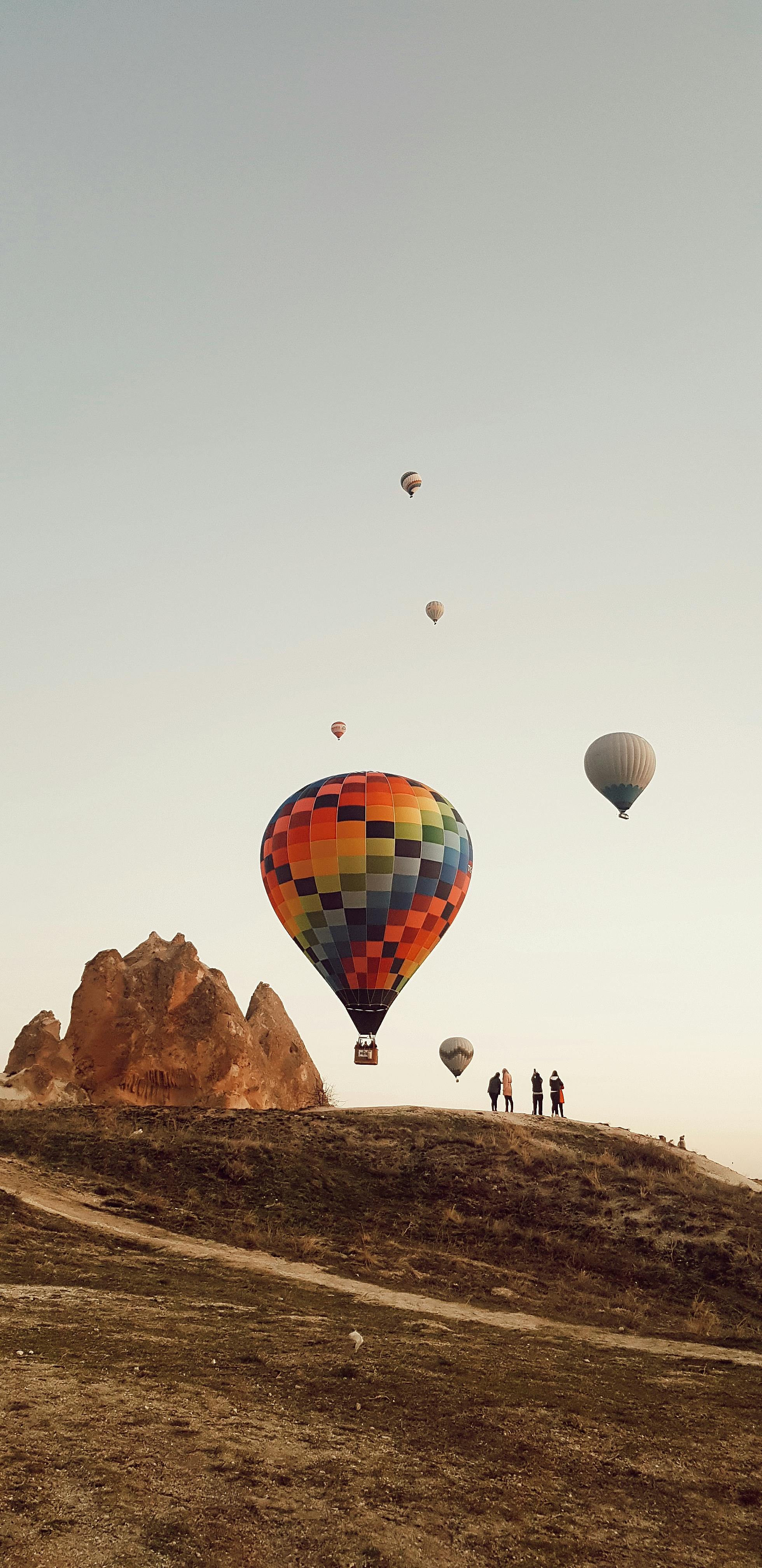 Colorful hot air balloons flying over Göreme at sunrise with unique rock formations.