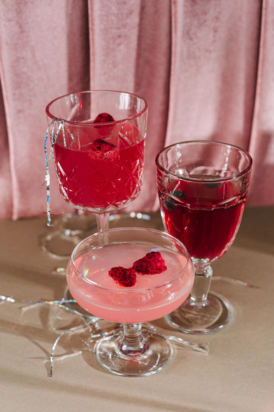 A stylish arrangement of pink and red cocktails garnished with raspberries in elegant glassware.