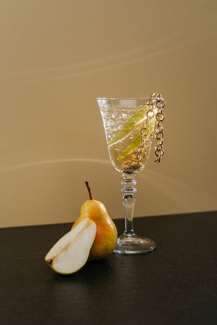 A sophisticated pear cocktail in a crystal glass adorned with a gold chain, perfect for classy occasions.