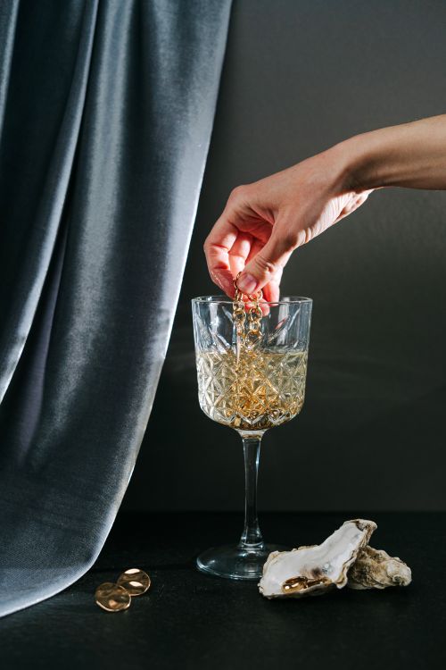 Free Artistic still life with a hand holding jewelry in a crystal glass, creating a luxurious scene. Stock Photo