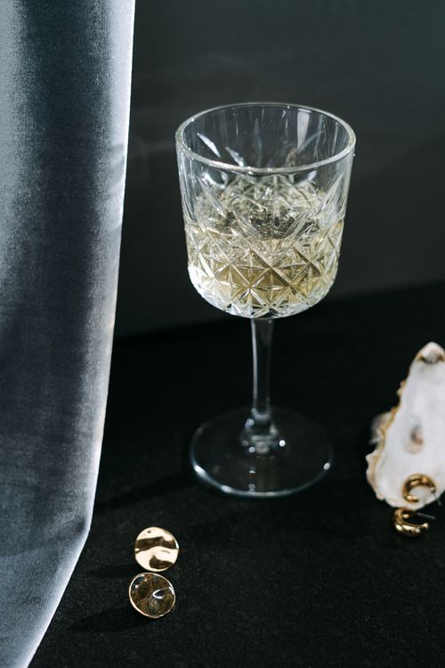 Free A sophisticated crystal glass filled with champagne beside pearls on a dark surface. Stock Photo