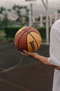 A close-up view of a basketball being held on an outdoor court, perfect for sports themes.
