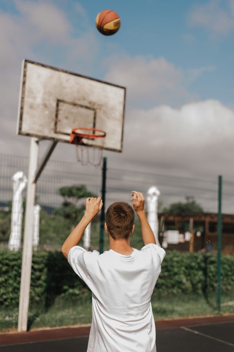 Back View Of A Man In A White Shirt Shooting A Basketball