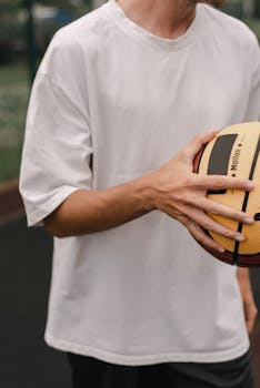 A cropped image of a man in a white shirt holding a basketball on an outdoor court.