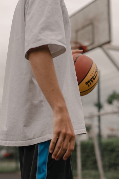 Person in White T-Shirt Holding Basketball Ball 