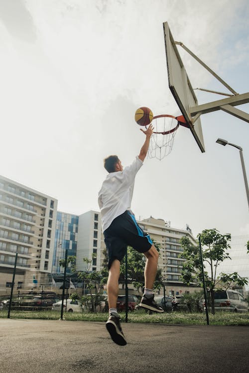 Photo of a Man in a White Shirt Performing a Layup