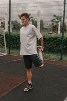 A man performs a leg stretch on an outdoor sports court, preparing for exercise.
