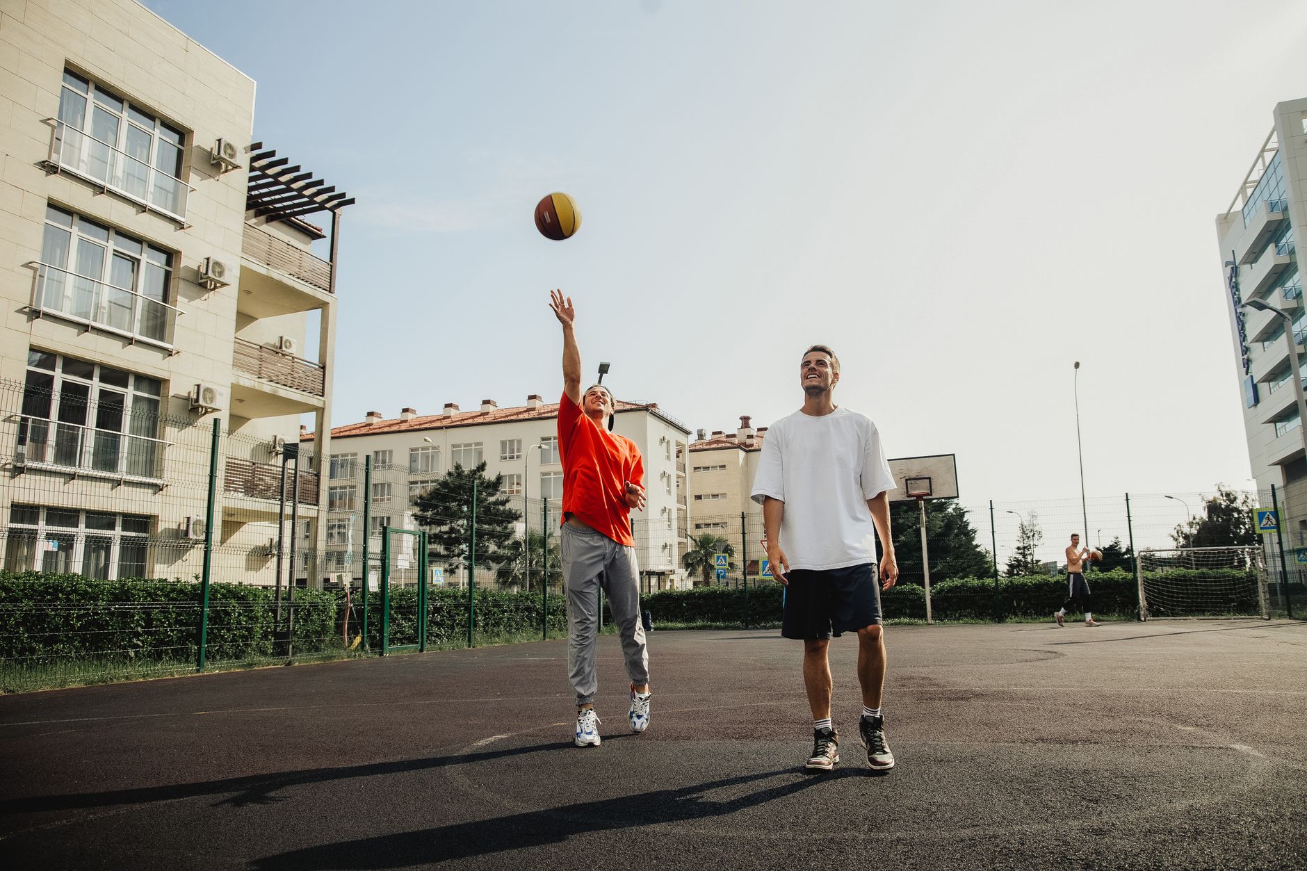 Two young men playing basketball on an outdoor urban court on a sunny day.