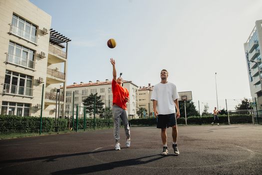 Two young men playing basketball on an outdoor urban court on a sunny day.