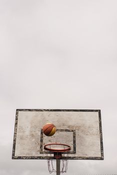 A basketball approaches the hoop against a cloudy sky, capturing the essence of outdoor sports.
