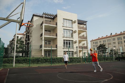 Two men playing basketball on an outdoor court surrounded by apartment buildings.