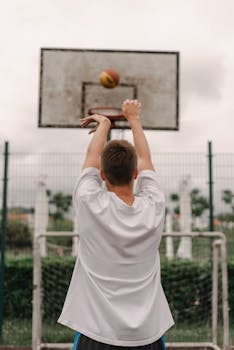 Man shooting basketball into hoop from behind on an outdoor court, showcasing perfect technique and stride.
