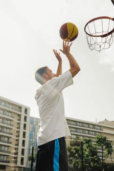 A young man in a white shirt shooting basketball on an outdoor court.