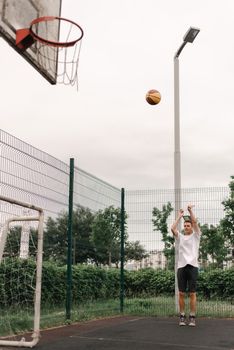A young man in active wear shooting a basketball on an outdoor court during the day.