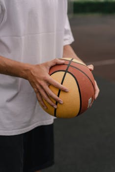 Close-up of a man holding a basketball on an outdoor court.