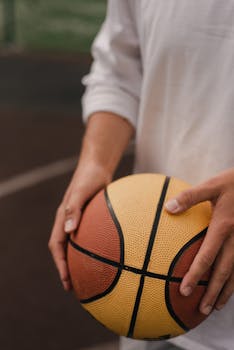 A man in a casual shirt holding a basketball on an outdoor court, emphasizing sports and leisure.