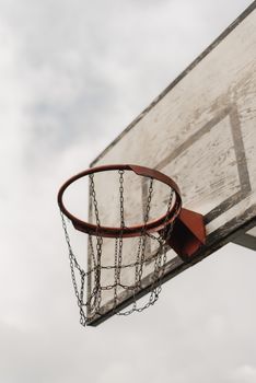 Close-up of a weathered basketball hoop with a chain net against a cloudy sky.