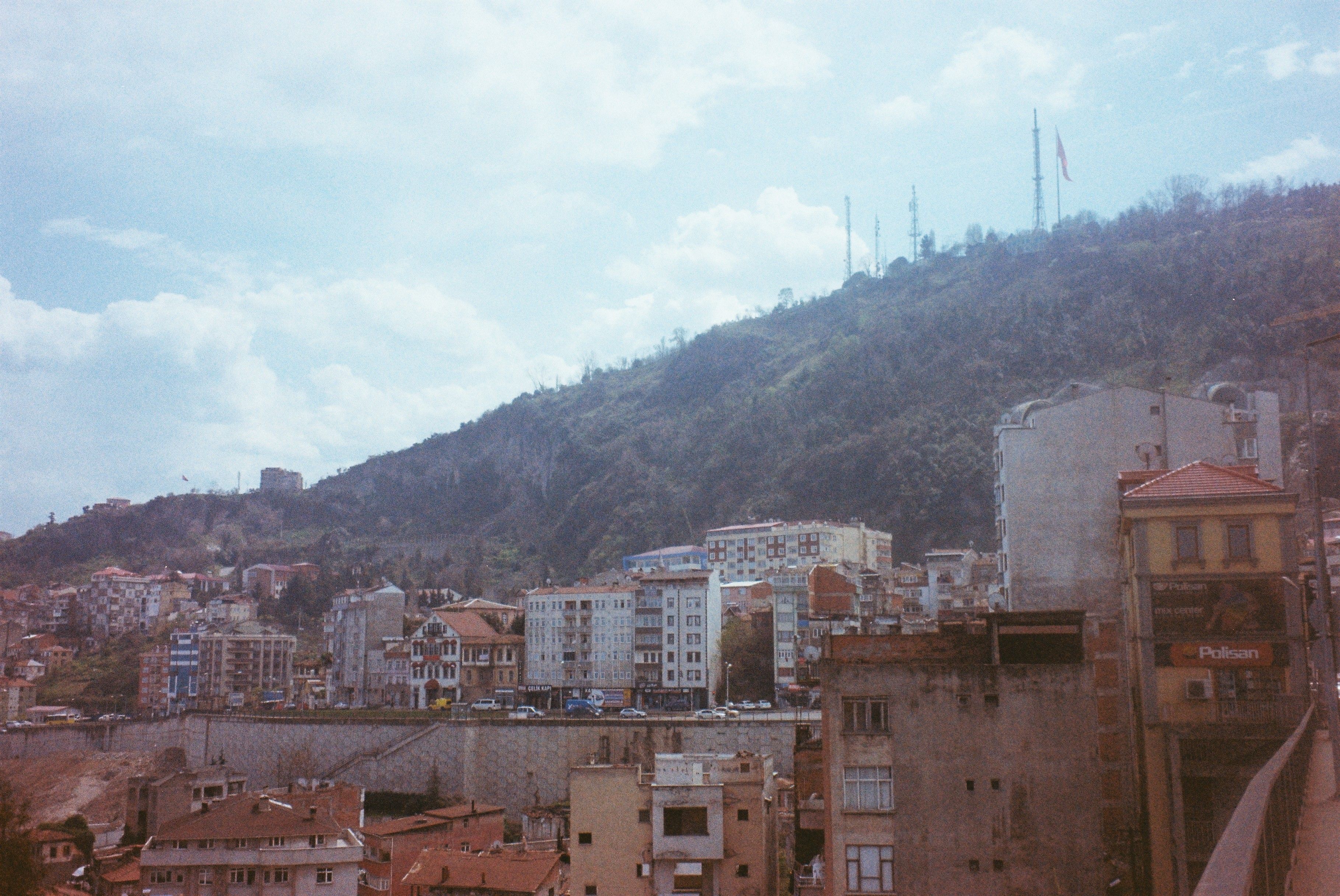Cityscape with buildings against a mountain landscape under a cloudy sky.