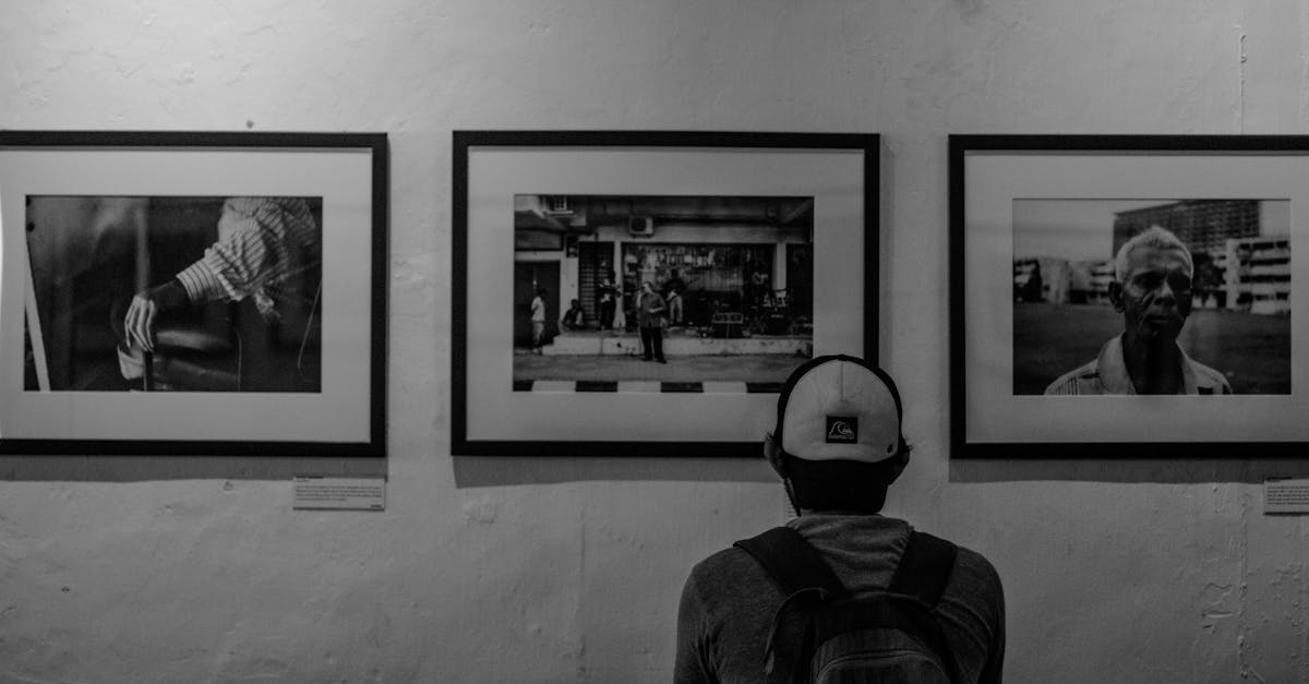 한글뷰어 다운로드 A man in a cap and backpack admires monochrome art in a gallery.