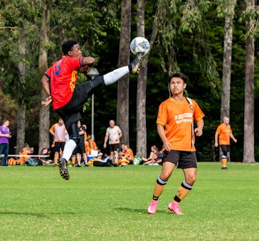 Exciting soccer game moment with athlete kicking the ball mid-air on a sunny day.