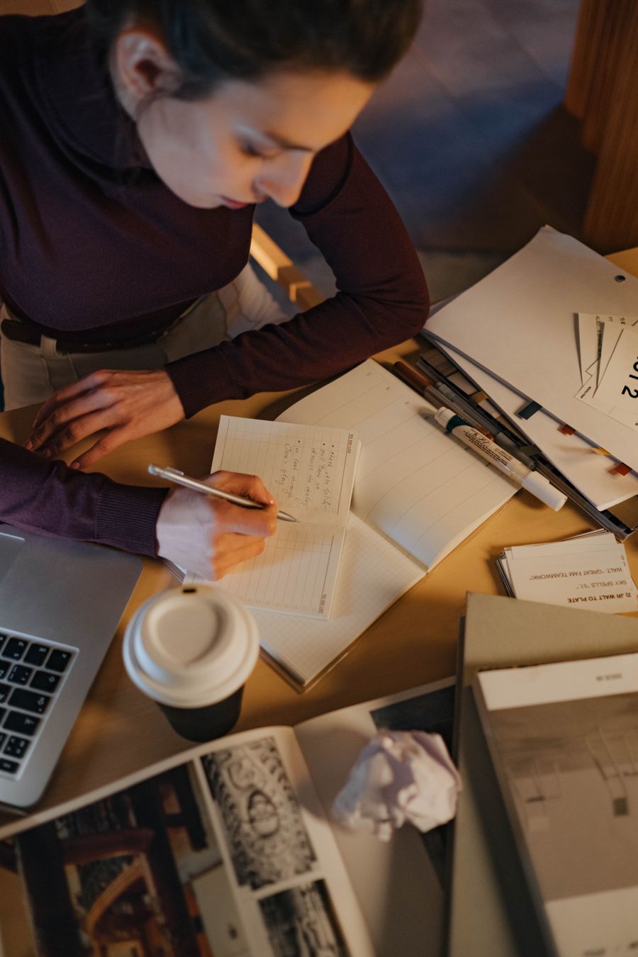 Overhead view of a woman writing notes beside a laptop and coffee