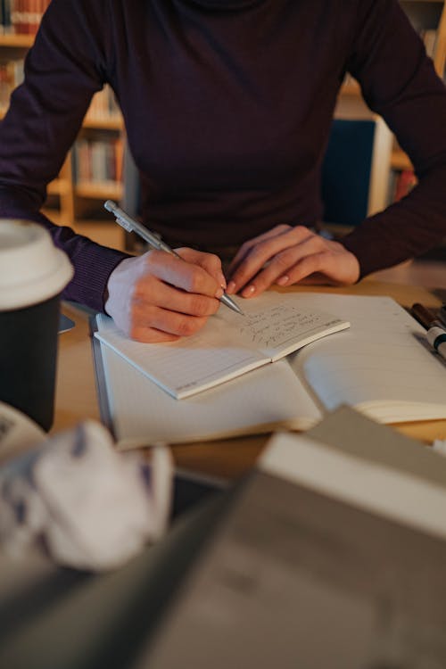 Person in Brown Long Sleeve Shirt Writing on White Paper